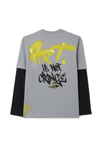 Grijze langemouwen shirt met zwarte mouwen met gele en zwarte graffiti-achtige tekst, waaronder "ART" en "is NIET CRINGE," en een handontwerp.