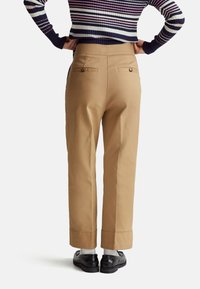 Khaki tapse broeken met een soepele textuur, voorzien van achterzakken met knopen en opgerolde manchetten, gecombineerd met zwarte schoenen en witte sokken.