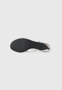 Sandaletta argento con un finish metallico liscio, suola in gomma nera e un design minimalista caratterizzato da cinture incrociate per un migliore supporto.