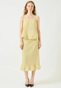 Vestido amarillo con pliegues, tirantes finos y dobladillo acampanado. Hecho de una tela ligera, presenta un diseño en capas y una textura suave.