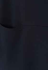 Mörk marinblått tyg med en slät yta, som har en böjd fickdetalj. Minimalistisk design med subtila sömmar.