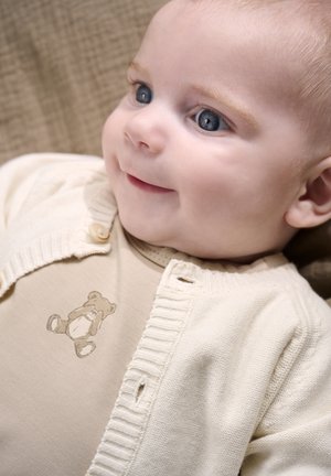 Lysebeige cardigan med ribkant over en tan romper med brun bjørneprint, der fremhæver bløde stoffer og subtile teksturer.