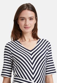 Gestreift Kleid mit einem Chevron-Muster in Marineblau und Weiß, mit V-Ausschnitt und kurzen Ärmeln, aus einem weichen, dehnbaren Stoff gefertigt.