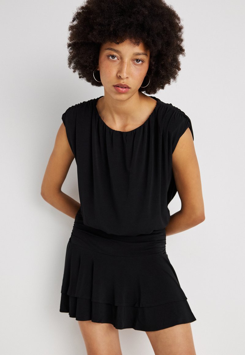 Vestido preto com mangas curtas e franzidas e saia rodada. Textura suave, cintura ajustada e detalhes de bainha em camadas.