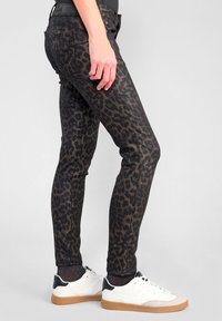 Svarta slim fit-jeans med leopardmönster. Blandmaterial av bomull, fem fickor och bärs med vita sneakers för en avslappnad look.