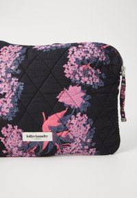 Quiltad svart påse med rosa och blå blommönster. Inkluderar en silverdragkedja och en etikett med varumärkesnamn. Mjuk tygtextur.
