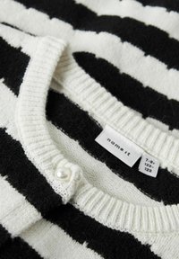 Svetr s černobílými pruhy a žebrovaným výstřihem, se sladěným bílým perlou a štítkem se jménem značky a velikostí.