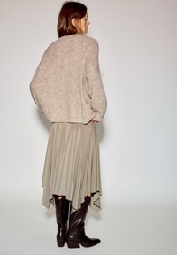 Svetlobéžový pletený sveter, béžová sukňa s vysokým a nízkym strihom s plynulým závesom a tmavohnedé kožené kovbojské čižmy s tvarovaným podpätkom.