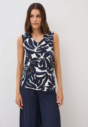 Sleeveless top in cream with a navy blue abstract leaf pattern. V-neck design, soft fabric, paired with loose navy trousers.