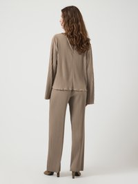 Maglia beige a maniche lunghe a coste e pantaloni larghi abbinati con una vestibilità rilassata. Tessuto texturizzato con sottili linee verticali; scarpe con tacco.