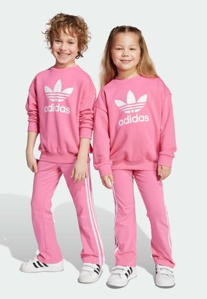 Felpe e pantaloni in cotone rosa, con logo bianco adidas e tre strisce. I bambini indossano sneakers bianche con dettagli neri.