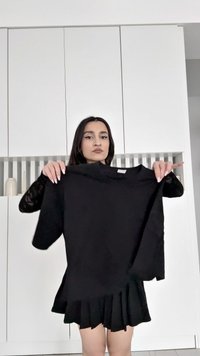 Fekete, rövid ujjú póló, kerek nyakkivágással, amelyet egy személy tart. Az anyag simának tűnik, egyszerű és letisztult dizájnnal.