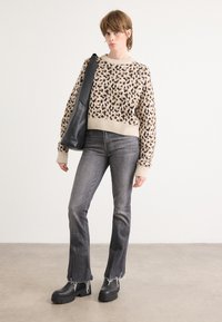 Beiger Pullover mit schwarzen Leopardenflecken, gerippter Halslinie, kombiniert mit dunkelgrauen, ausgestellten Jeans mit ausgefransten Säumen und schwarzen klobigen Stiefeletten.