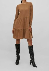 Abito a maniche lunghe, a coste, di colore marrone chiaro con gonna a strati. Abbinato a stivali neri alti fino al ginocchio con tacco a stiletto. Texture liscia, design semplice.