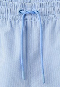Ceinture élastique bleu clair avec cordon assorti noué en un simple nœud sur un tissu bleu pâle texturé.