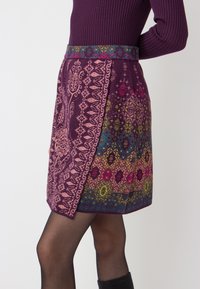 Knee-length skirt in rich purple fabric featuring intricate floral and geometric patterns in pink, green, and blue, with a woven waistband.
