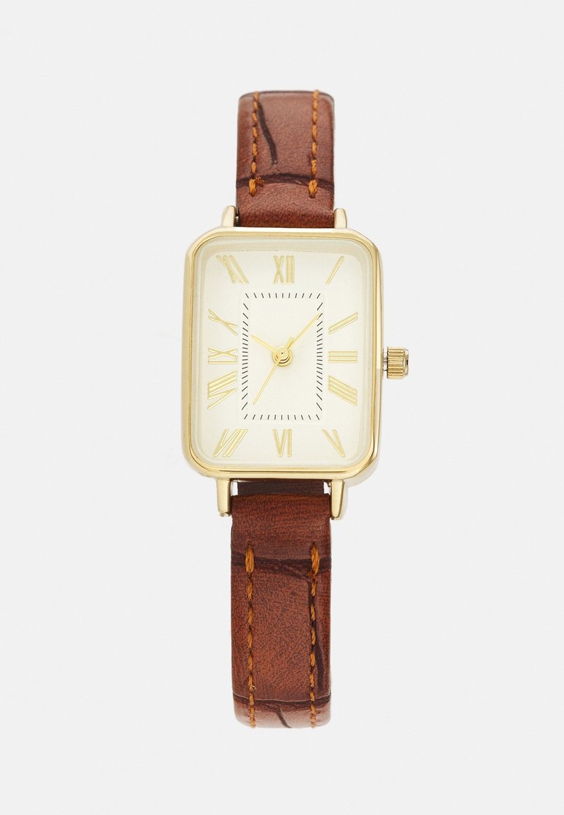 Montre rectangulaire en or avec cadran crème, chiffres romains dorés et bracelet en cuir marron avec couture visible.