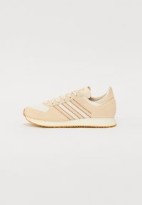Beige sportcipő velúr és hálós anyagból, három texturált csíkkal, kerek orral és gumis kivitelű talppal.