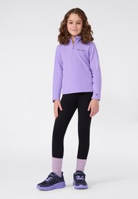 Pullover viola in pile con mezza zip e logo, abbinato a leggings neri e sneakers con accenti viola. I calzini sono di un leggero viola a coste.
