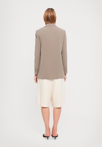 Lys grå blazer med skreddersydd passform, myk tekstur, en-rokks design og knappede mansjetter, kombinert med kremfargede shorts.
