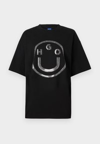 Camiseta de manga corta negra con un diseño de logo en purpurina plateada que incluye texto, hecha de algodón, con un corte relajado y cuello redondo.