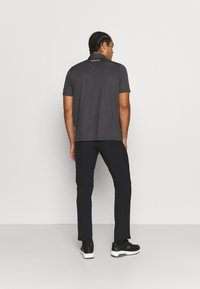 Polo cinza de mangas curtas; a vista traseira mostra um logótipo na parte do pescoço. Combinado com calças pretas justas e sapatilhas pretas.