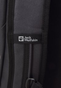 Sivý batoh z látky s textúrovaným povrchom, s čiernymi kontrastnými detailmi a bielym logom Jack Wolfskin s ikonou paw na nálepke.