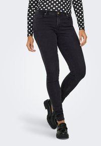 Jeans ajustados negros con una textura suave, que presentan un diseño clásico de cinco bolsillos y un cierre de botón; combinados con mocasines negros.