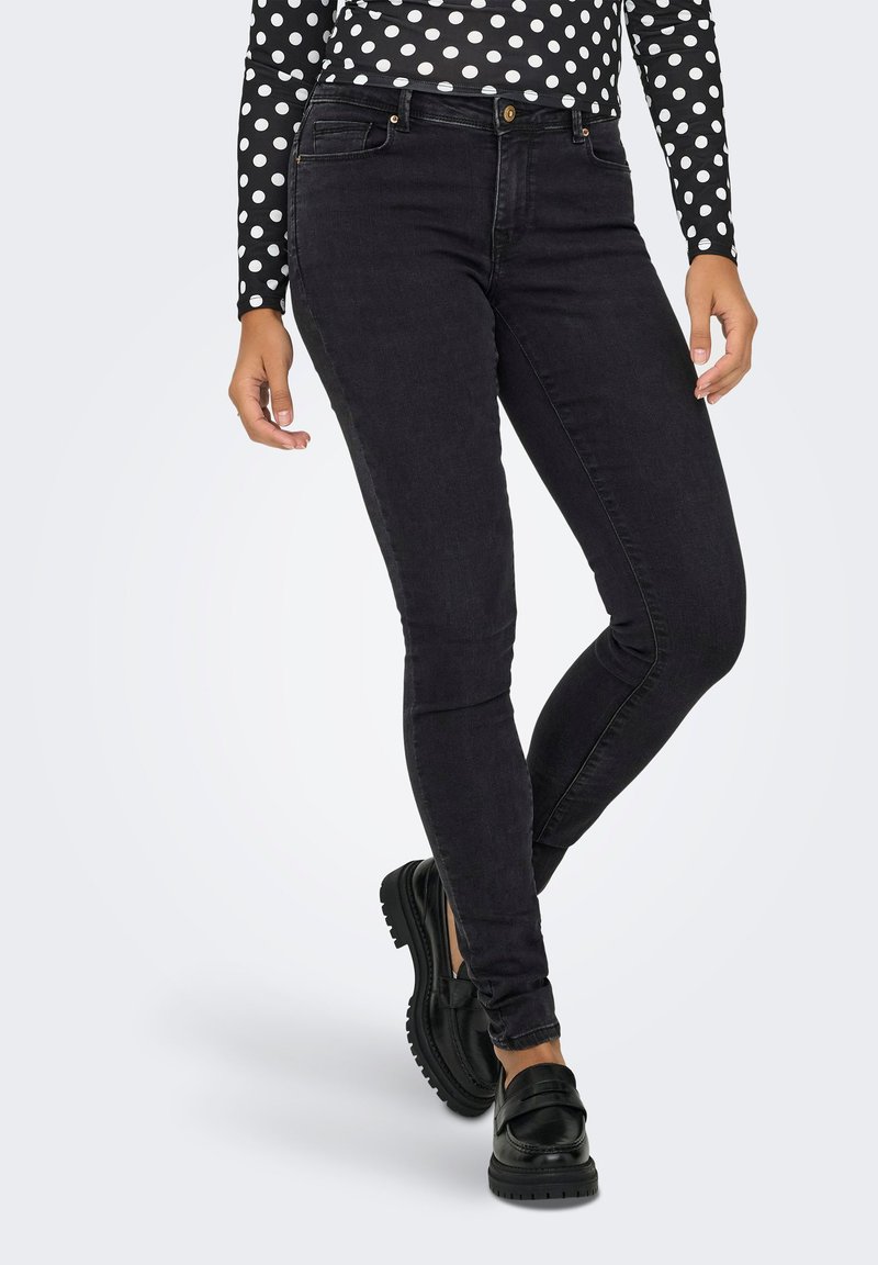 Jeans ajustados negros con una textura suave, que presentan un diseño clásico de cinco bolsillos y un cierre de botón; combinados con mocasines negros.