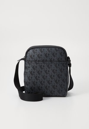 Kleine zwarte crossbodytas met donkergrijs geometrisch patroon en verstelbare band, getoond tegen een witte achtergrond.