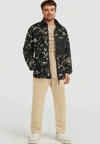 Black and white fleece jacket with a zippered chest pocket, featuring a textured pattern. Paired with beige trousers and white sneakers.