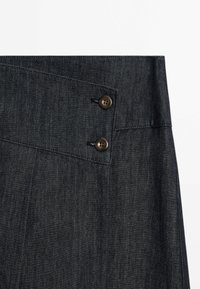 Jupe en jean gris foncé avec détail taille haute et deux boutons foncés sur un rabat en tissu superposé.