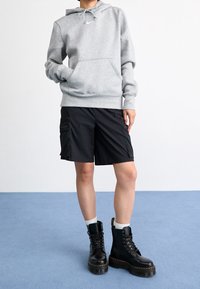 Grå huvtröja med framficka och dragsko, ihop med svarta shorts som har sidofickor och svarta snörkängor med tjocka sulor.