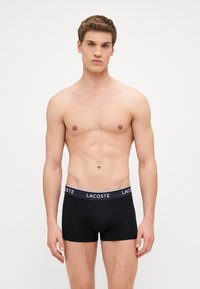 Czarne bokserki z białym elastycznym pasem z logo "LACOSTE". Gładki materiał z dopasowanym krojem i krótkimi nogawkami.