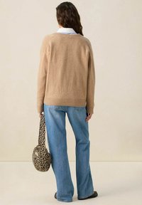 Pull en maille marron clair à coupe décontractée, avec un ourlet côtelé, associé à un jean évasé bleu clair et un sac à imprimé léopard.