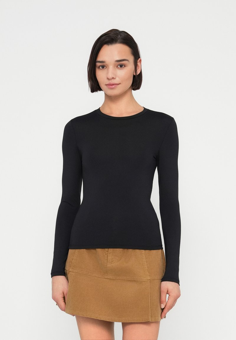 Μαύρο τοπ με μακριά μανίκια από λείο ύφασμα, με στρογγυλή λαιμόκοψη και εφαρμοστή γραμμή, σε συνδυασμό με φούστα από χακί κορντόρι με ίσια γραμμή.