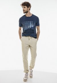 Námořnické bavlněné tričko s grafikou hor, béžové kalhoty s šňůrkou a světlé tenisky s akcenty. Jednoduchý design, uvolněný střih.