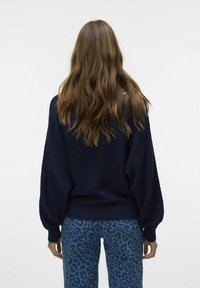 Pull en maille côtelée bleu marine avec des manches volumineuses, associé à un jean imprimé léopard bleu, mettant en avant une coupe décontractée et un tissu texturé.