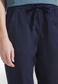 Granatowe spodnie z obwodem w talii na sznurek, wyposażone w dwie przednie kieszenie i gładką fakturę. Zaprojektowane z myślą o komforcie i łatwości noszenia.