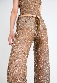 Bronze, sequined two-piece outfit featuring a fitted top and wide-leg pants with a textured finish and decorative tassel detail at the waist.