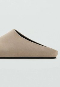 Scarpa slip-on in suede beige con un design minimalista, caratterizzata da una superficie liscia e una punta arrotondata, poggiata su una suola nera.