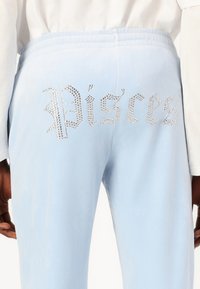 Pantaloni jogger in velluto azzurro chiaro con un design "Pesci" arricchito di cristalli sul retro, caratterizzati da una texture liscia e una cintura elastica.