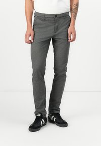 Graue Slim-Fit-Hosen aus strukturiertem Stoff mit Knopfverschluss, seitlichen Taschen und einem schlichten Design, kombiniert mit schwarzen Sneakers.