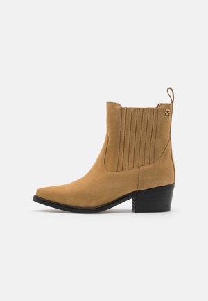 Botín de ante en color marrón claro con puntera afilada, paneles laterales acanalados y tacón ancho negro. Cuenta con una lengüeta para facilitar su puesta.