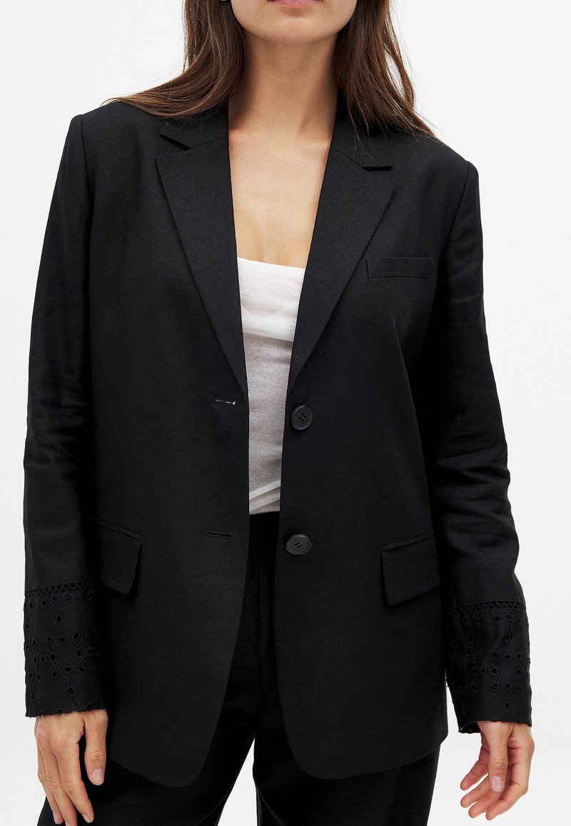 Black blazer with a tailored fit. Features two buttons, side pockets, and embroidered black cuffs. Made from lightweight fabric.