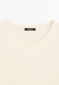 Maglione di colore crema a maglia con scollo rotondo, bordi a coste e un'etichetta nera con la scritta "Massimo Dutti". Texture morbida e design leggero.