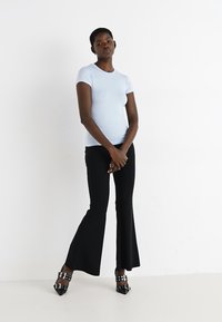 T-shirt aderente di un azzurro chiaro abbinato a pantaloni neri a zampa d'elefante. I pantaloni hanno una finitura testurizzata e sono indossati con scarpe con tacco nere lucide.