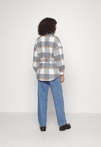 Camisa de cuadros gris y blanca con acentos naranjas, ceñida a la cintura; combinada con jeans rectos azul claro y zapatos negros.