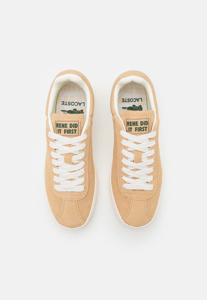 Zapatillas de ante color marrón con cordones blancos y suelas de goma. Presentan texto verde en la lengüeta. Punta redondeada y diseño minimalista.