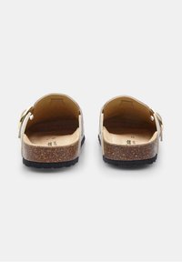 Back view of beige cork sandals with leather straps and gold hardware, featuring a textured footbed and dark rubber outsole.